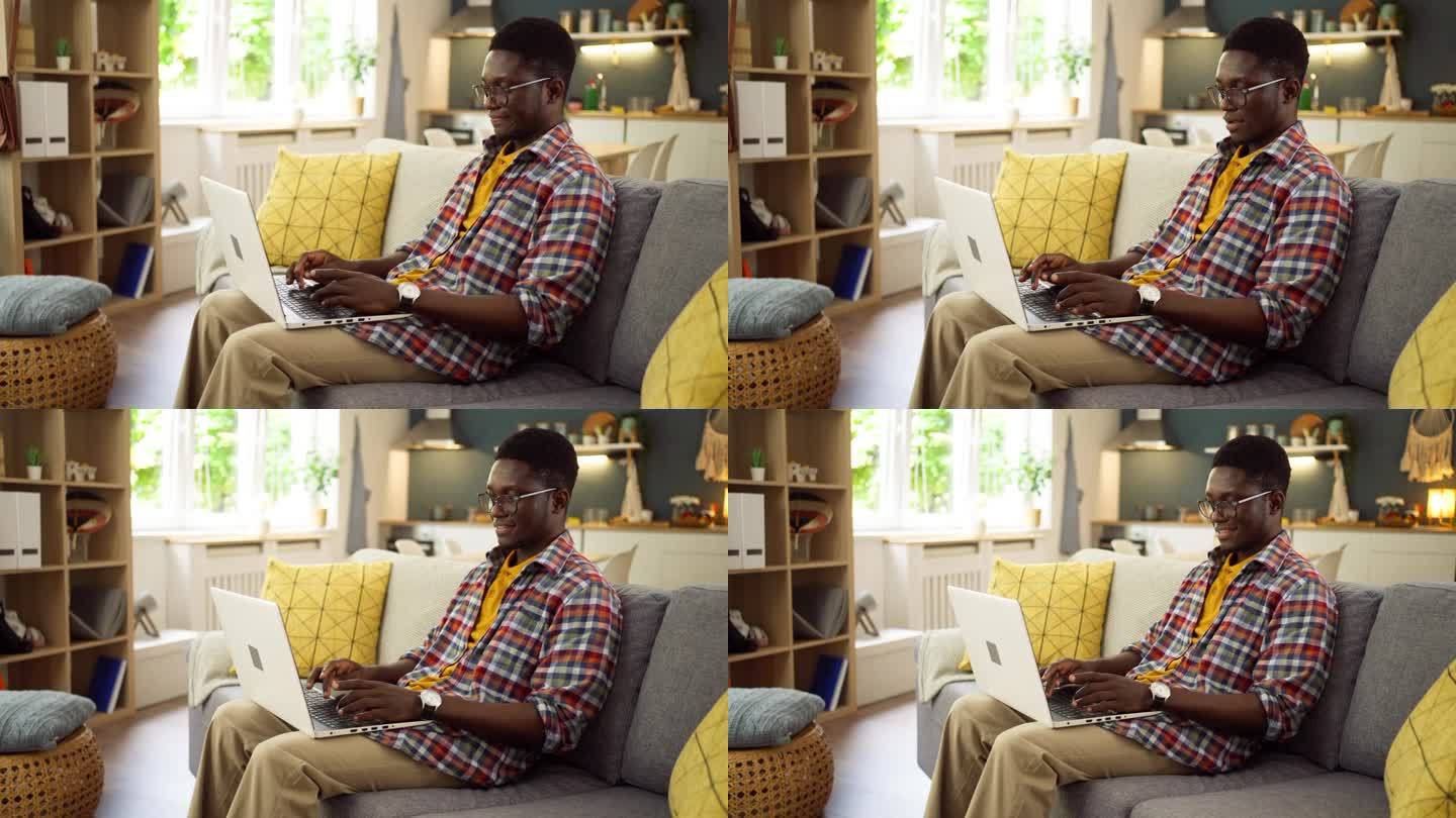 年轻的非洲裔美国人坐在沙发上用笔记本电脑工作