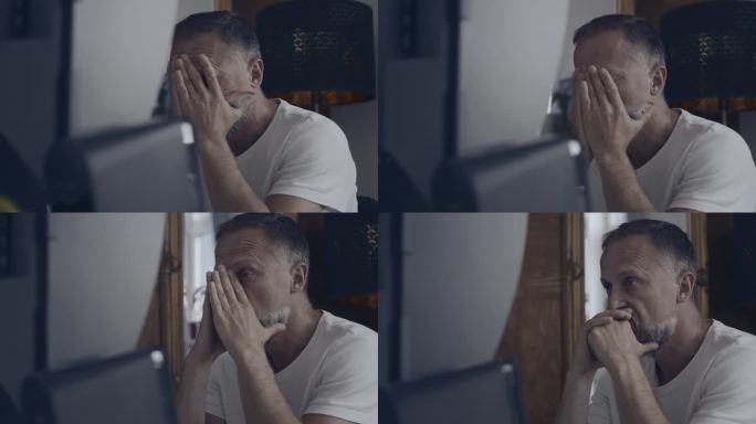 沮丧的男人独自坐在电脑屏幕前，双手捂着脸。工作倦怠和焦虑