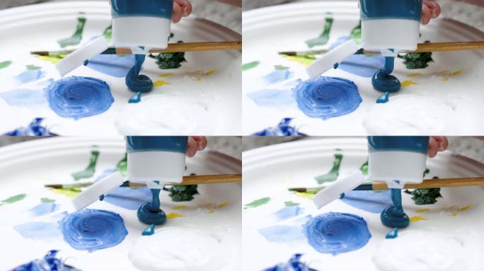 特写深蓝色颜料从瓶子里倒出来，把颜料挤进调色板，因为有一只手坐着挤颜料准备在绘画中使用，油漆盘上有一