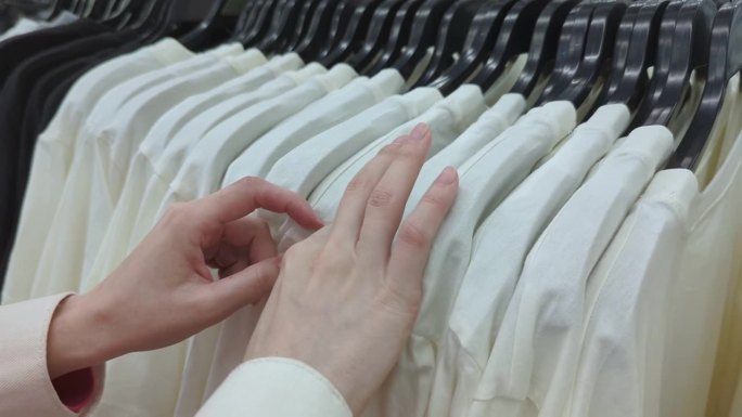 特写镜头的女人正在挑选衣服的商店与t恤。购物日和大减价。