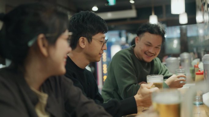 三个亚洲游客，晚上在一家餐馆享受他们在这座城市的时光。
