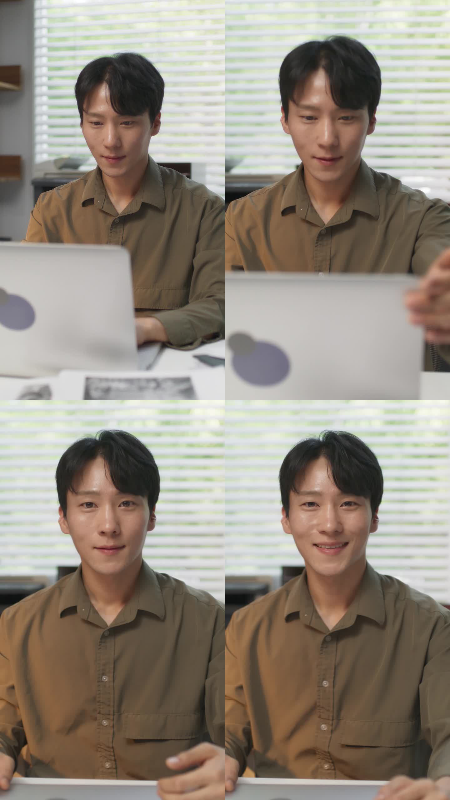 垂直屏幕:一位帅气的韩国男性在一家时尚创意机构的办公桌后对着电脑工作。快乐的年轻人合上他的笔记本电脑