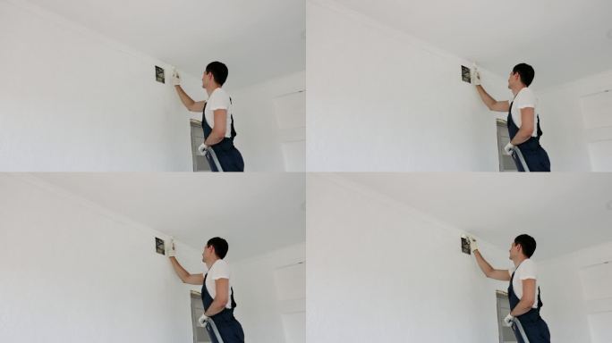 穿制服的修理工用刷子把墙壁刷成白色