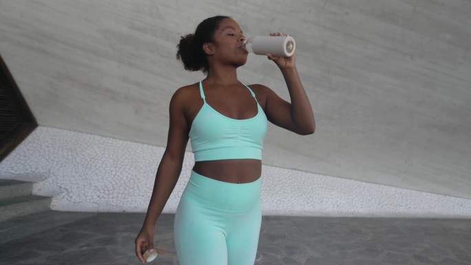 年轻的非洲妇女在户外锻炼时休息喝水-运动人的生活方式概念