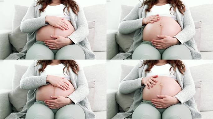 在怀孕的最后阶段，孕妇坐在沙发上轻轻按摩她的腹部，期待着宝宝的到来。