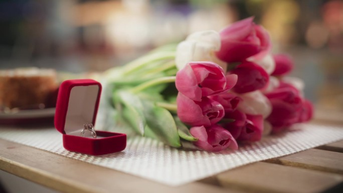 订婚静物概念与闪闪发光的结婚戒指与宝石。静态镜头与珠宝在一个红盒子上的木桌与美丽的粉红色花束与郁金香