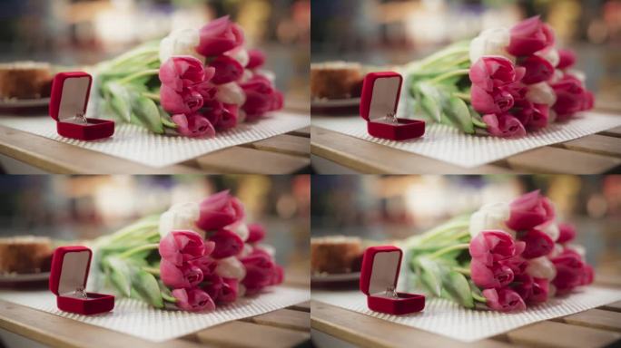 订婚静物概念与闪闪发光的结婚戒指与宝石。静态镜头与珠宝在一个红盒子上的木桌与美丽的粉红色花束与郁金香