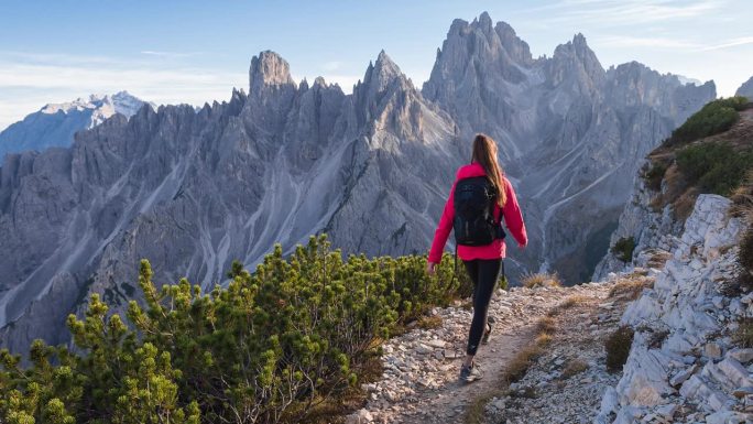 健康的女人征服山路，周围是令人敬畏的山峰