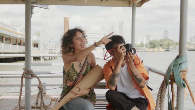 年轻的游客在曼谷湄南河上乘坐渡轮时，很高兴地观看和拍照。