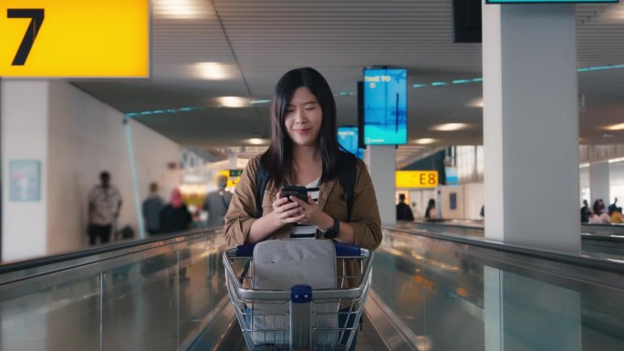 在机场人行道自动扶梯上使用手提电话的亚洲女旅客