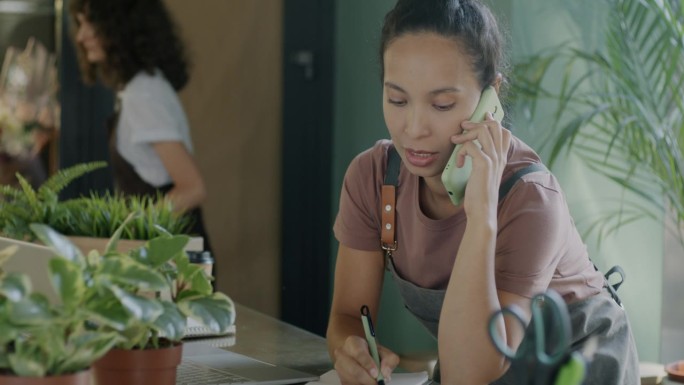 在花店销售盆栽植物的女企业家用手机与客户交谈
