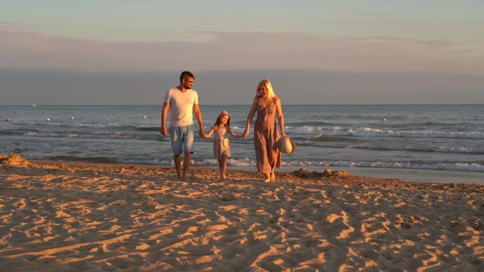 日落时分，一家人带着孩子在海边的沙滩上散步。暑假、旅游