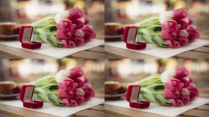 一枚漂亮的订婚戒指，上面有一颗大宝石，放在桌子上的红色盒子里，旁边是粉红色的郁金香花束。浪漫求婚的鲜