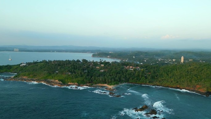 绿色的热带岩石岛在蓝绿色的海洋中间被海浪冲刷垂直鸟瞰。由无人机拍摄的画面显示，斯里兰卡密里萨的秘密海
