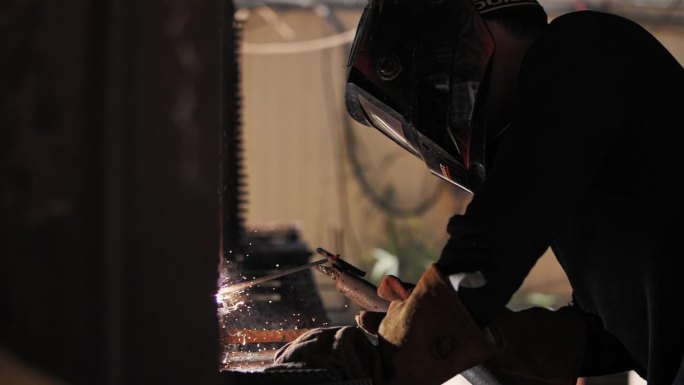 焊工在建筑工地为整体工程焊接金属棒的焊工。焊接产生火花和烟雾。