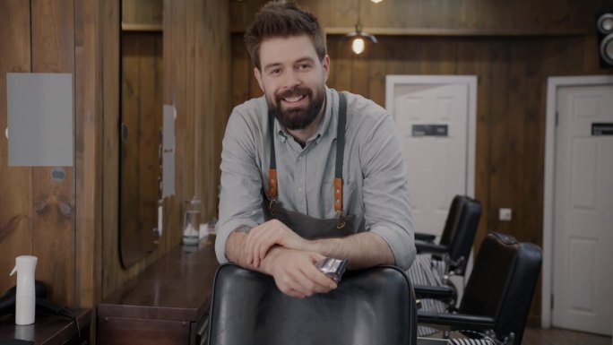 熟练的男理发师站在工作室拿着剃须机微笑着看着镜头的肖像