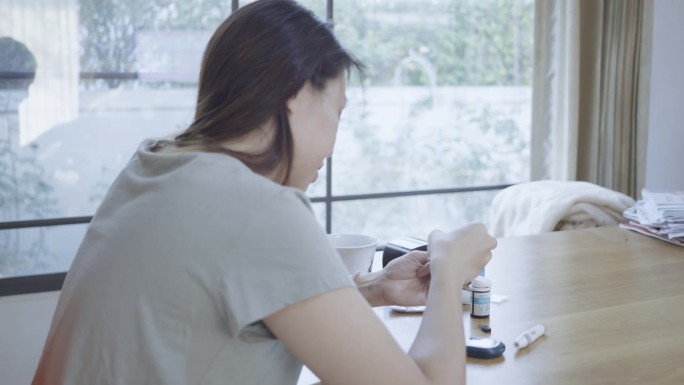 一名患有糖尿病的东南亚妇女在家中使用血糖自测仪检查血糖