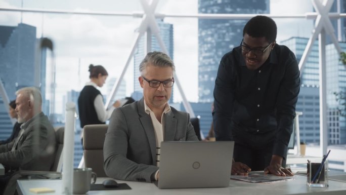 在市中心明亮的摩天大楼办公室里，成功的非裔美国男性首席执行官与手提电脑后面的资深交易员交谈。黑人和白