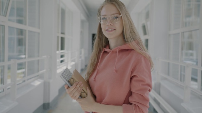 美丽的年轻女学生站在大学大厅拿着书微笑着看着镜头的慢动作肖像