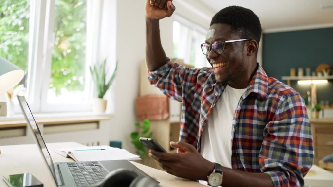 非裔美国男学生在笔记本电脑上看到考试成绩后庆祝考试通过