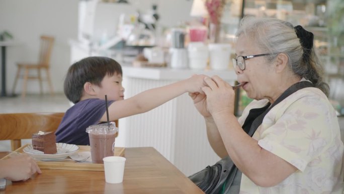 一位亚洲祖母和她的孙子正在蛋糕店一起吃巧克力蛋糕。