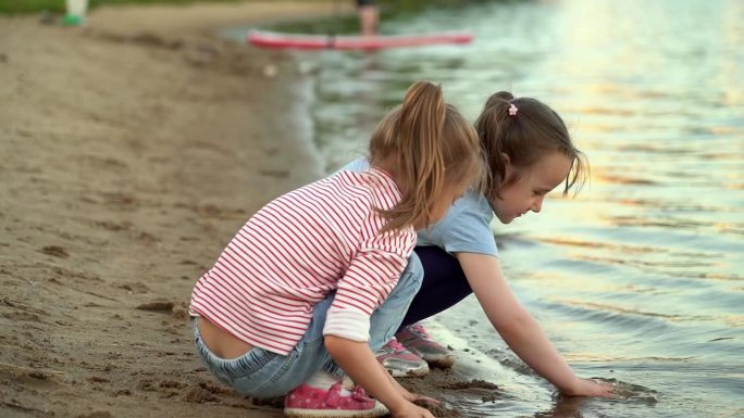 傍晚夕阳下，女孩们在夏日公园的河岸上玩沙。