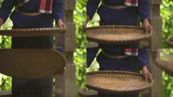 一位年长的亚洲妇女手持竹篓或藤篓筛稻谷，将稻谷和稻壳分开。
