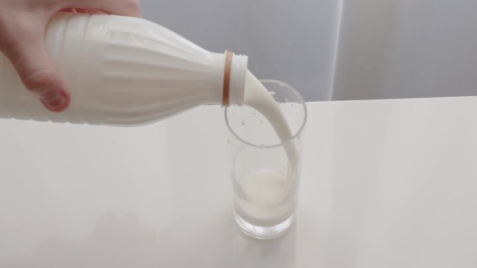 一个男人把鲜牛奶倒进一个透明的玻璃杯里。一个男人喝了一种乳制品，用塑料瓶装的牛奶