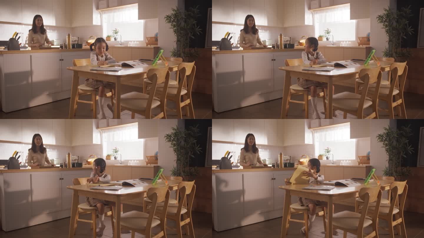 一个韩国女孩坐在厨房的桌子上画画，而她的母亲正在准备早餐。上学前等待营养餐的可爱小女孩
