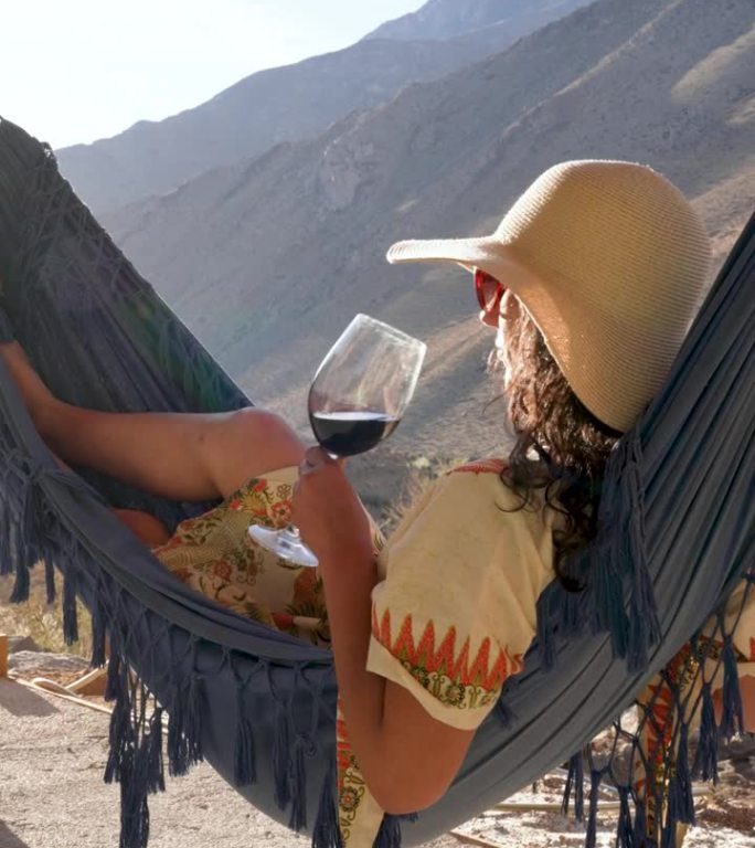拉丁美洲妇女躺在吊床上喝着酒，看着日落放松