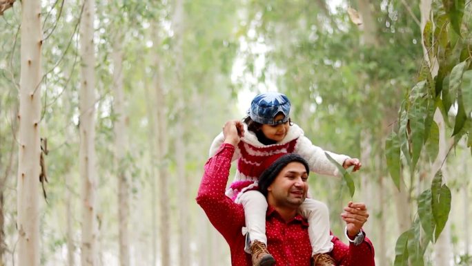 父亲背着女儿在森林里散步的正面照片。父亲抱着女儿沿着森林小径徒步。父亲和女儿一起在森林小径上徒步旅行