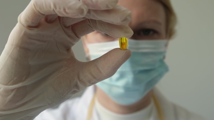 戴着白手套的女医生或药剂师的手拿着黄色的欧米伽3胶囊