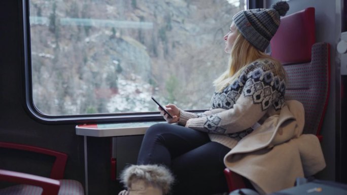 一名妇女在乘坐火车穿越冬季乡村时使用手机