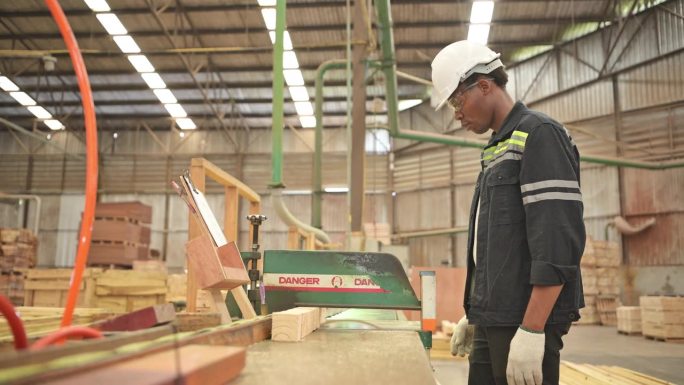 一名年轻的工人在一家木工工厂工作，使用木材锯床和切割机生产用于制作托盘的木片