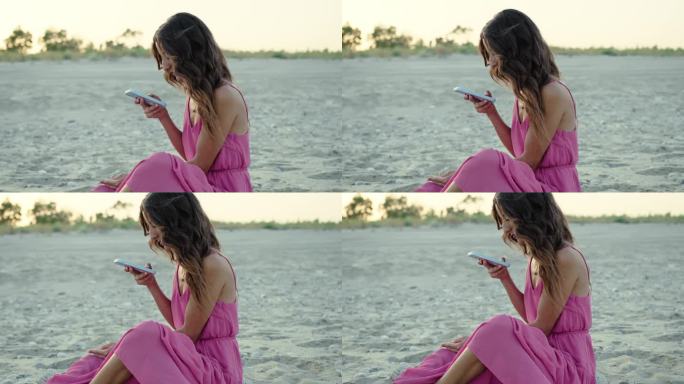 穿着粉色裙子的女孩在海边的沙滩上使用手机