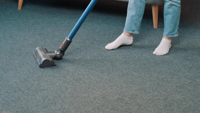 现代公寓中吸尘机吸尘地毯的近照。年轻女子在家客厅里保持房间整洁
