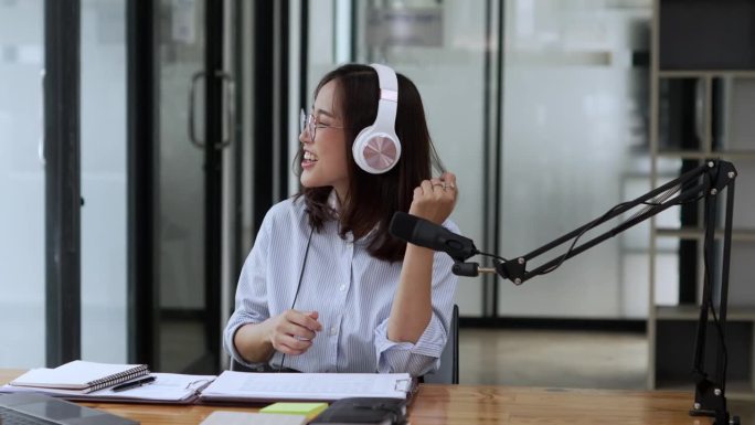 一名亚洲女性戴着耳机在笔记本电脑上录播客。女播客在她的家庭工作室制作音频播客。