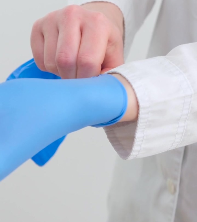 两副蓝色医用外科手套，在白底上用手绝缘。生产橡胶手套时，人的手戴的是乳胶手套。医生或护士戴丁腈防护手