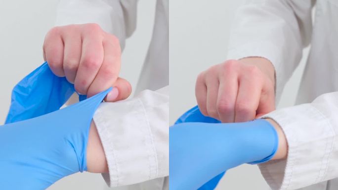 两副蓝色医用外科手套，在白底上用手绝缘。生产橡胶手套时，人的手戴的是乳胶手套。医生或护士戴丁腈防护手