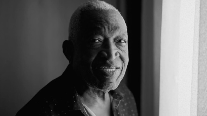 黑白单色摄影，一个黑人老人站在窗前看着相机的肖像