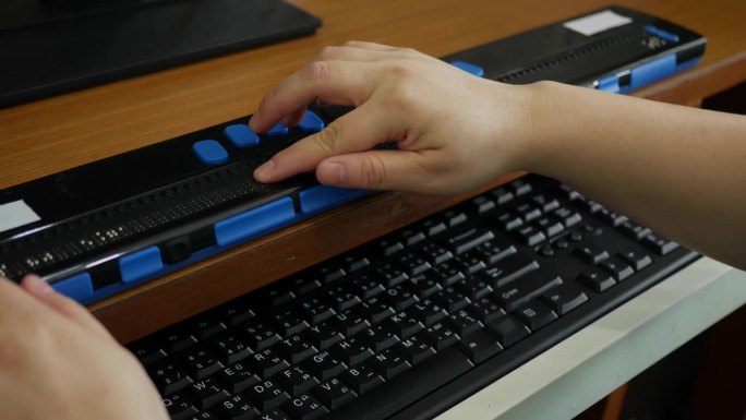 视障人士使用电脑键盘及盲文显示器或盲文终端机(视障人士的技术辅助装置)拍摄的近距离手掌