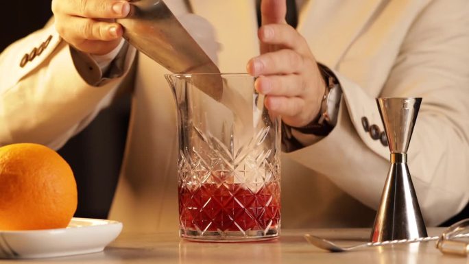 调酒师将冰块倒入调酒杯中，调制一杯内格罗尼鸡尾酒