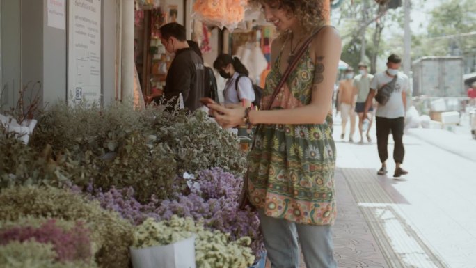 欢快的游客在曼谷花市散步，用智能手机给花拍照。