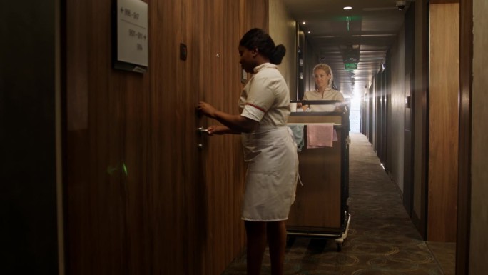 两名服务员在酒店房间的手推车上送干净的床单