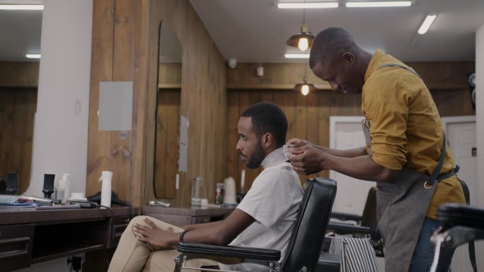一个非洲裔美国人在理发店里坐在镜子前的椅子上准备理发