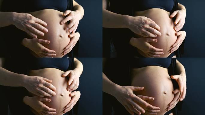 怀孕的妈妈穿着内衣，赤裸着圆圆的肚子，爸爸顽皮的手牵着她。怀孕最后一个月，第36周。侧视图。黑色背景