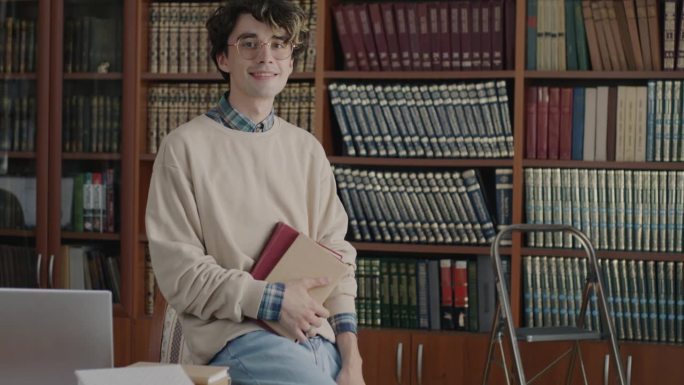 在大学图书馆里，一个聪明的年轻学生拿着书，带着淡淡的微笑看着镜头的慢动作肖像