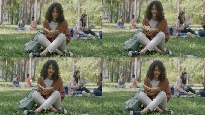 悠闲的年轻女子坐在公园的草坪上读着有趣的书，面带微笑