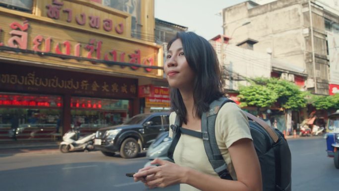 年轻的亚洲女性背包客在城市街道上使用手机。假日度假旅行。