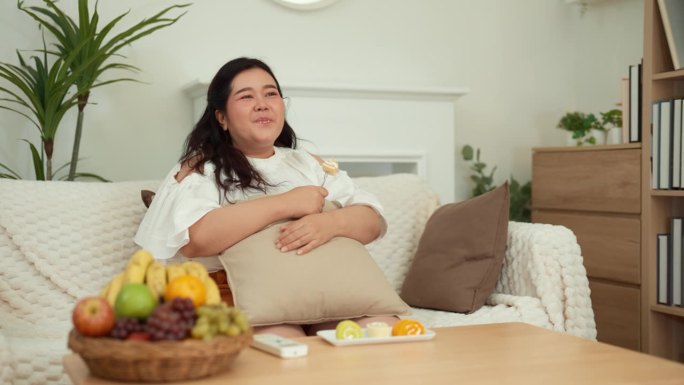 周末，一位肥胖的亚洲年轻女性坐在沙发上看电视节目。